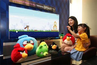 A picture of a child and their parent playing Angry Birds on a large screen, with plushes of the characters placed prominently